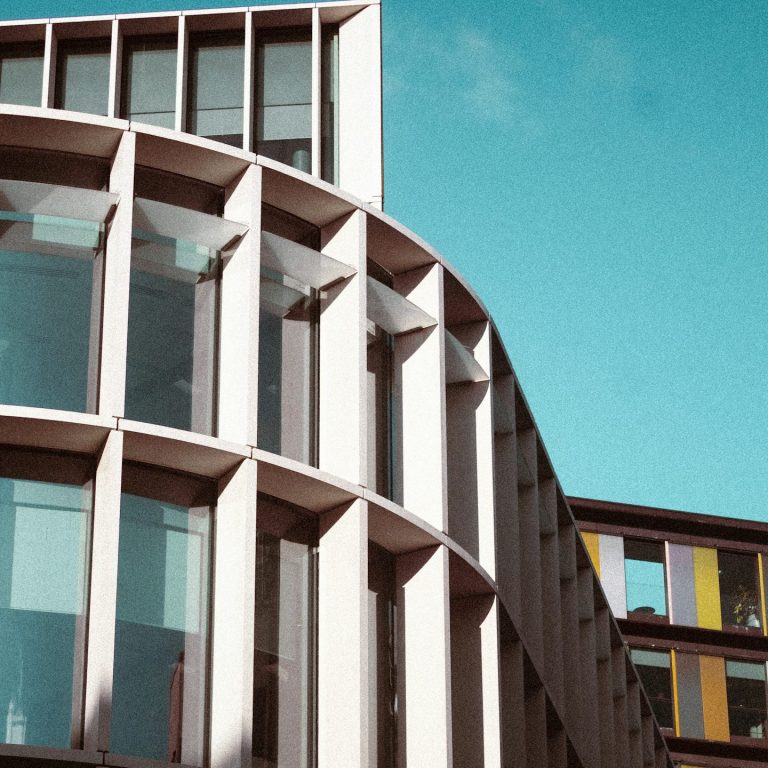 ¿Por Qué Elegirnos? Edificio moderno con fachada curva y grandes ventanales bajo un cielo azul.