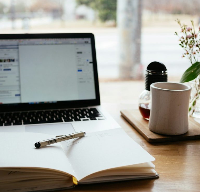 Intermediación de Empresas Portátil sobre una mesa con una libreta, un bolígrafo y una taza de café.